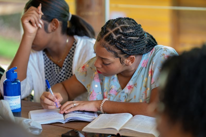 A young women takes notes in a For the Strength of Youth guide with her scriptures besisde her on a table in the Dominican Republic in July 2025.