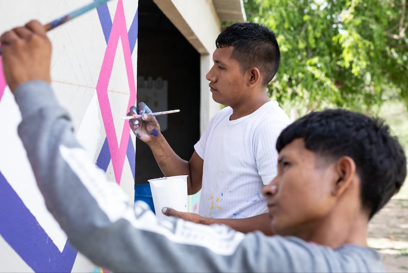 Keiber Epinayu, back, paints ancient Kanaas symbols on water infrastructure with a Wayúu youth in La Guajira, Colombia in February 2024.