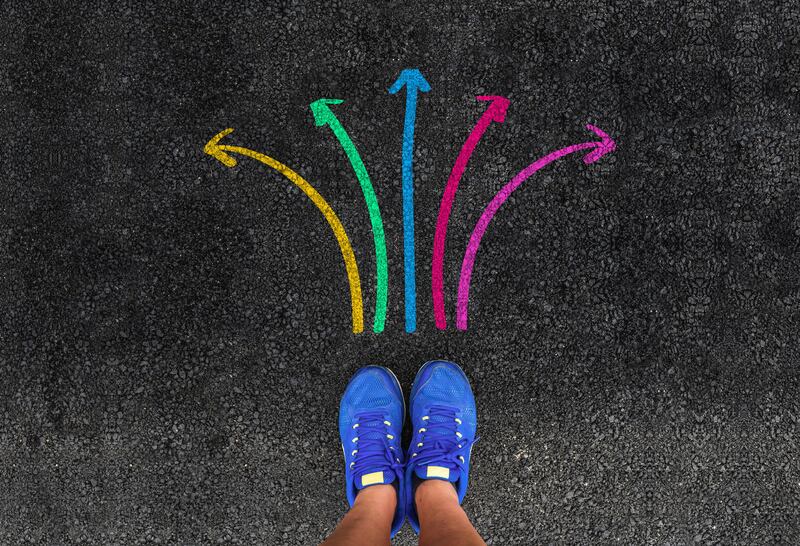 A person's standing next to five colorful direction arrow choices.