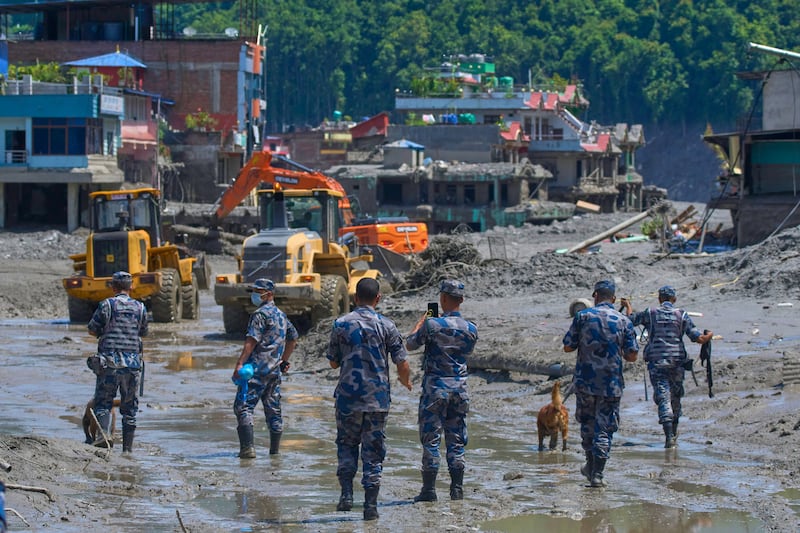 Nepalese policemen watch as earthmovers clear the debris of flash flooding in Nepal's Nuwakot district, Thursday, Aug. 27, 2026.