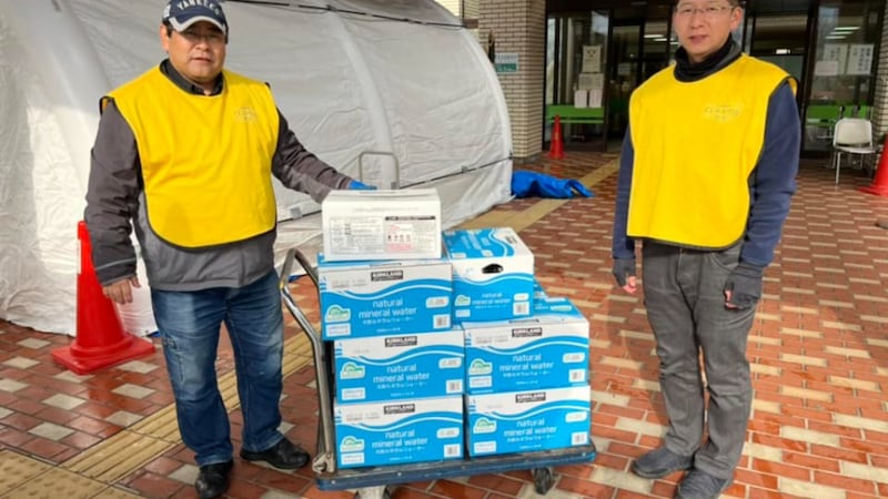 Two Church Welfare and Self-Reliance representatives wearing yellow Helping Hands vests donate cases of drinking water in Nanao, Japan.