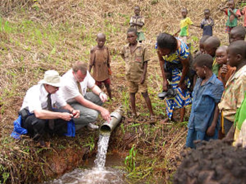Local children watch as Elder David Frandsen, a Church service missionary and water engineer, and Ro
