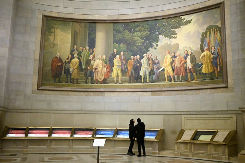 Two visitors look at exhibits beneath a large wall mural showing the signing of the Declaration of Independence at the National Archives Thursday, Jan. 29, 2026, in Washington, D.C.