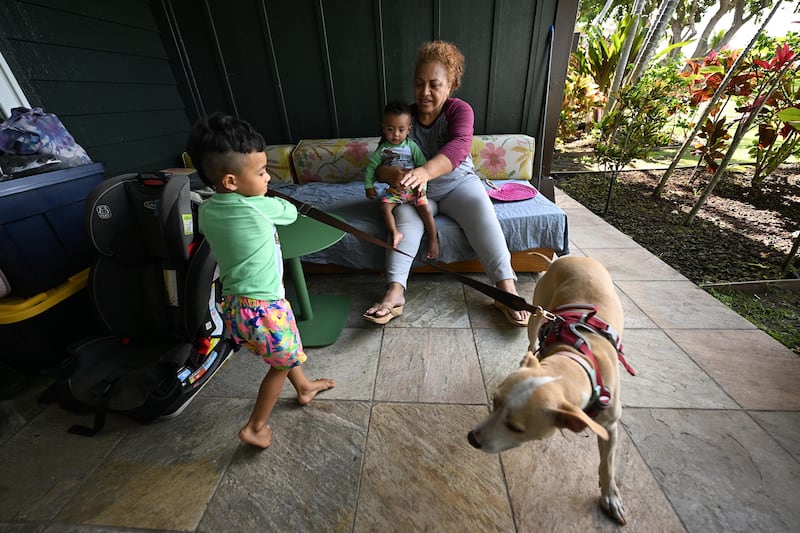 Etina Hingano holds her baby grandson as another grandson plays with their dog in a beach bungalow in Lahaina, on the island of Maui in Hawaii.