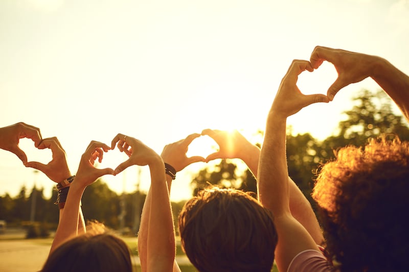 Hands of group friends in the shape of a heart against the sunset. Love and relationship friendship concept