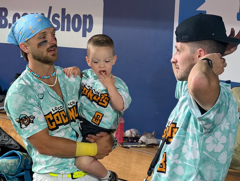 Kaden Bowler, left, of the Loco Beach Coconuts, holds his nephew, Preston Bowler, while talking to his brother, Branson Bowler, in the dugout of a game in Las Vegas, Nevada, on Friday, May 1, 2026. The Coconuts are one of six teams in the Banana Ball Championship League.