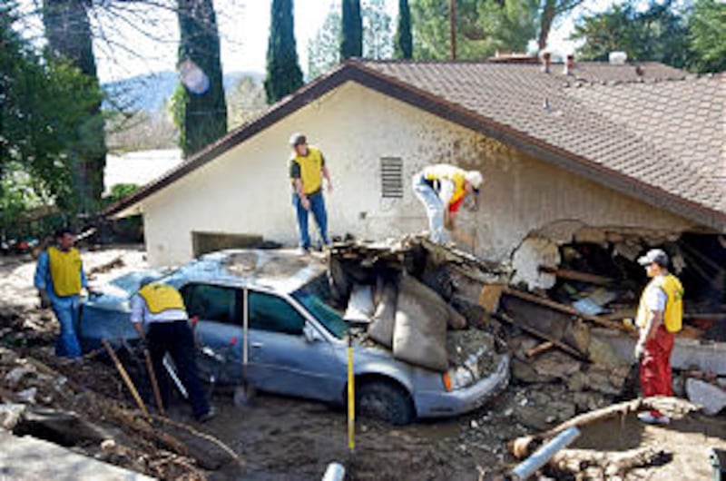 Wearing their "Helping Hands" vests, Church volunteers help dig a car out from under part of a house