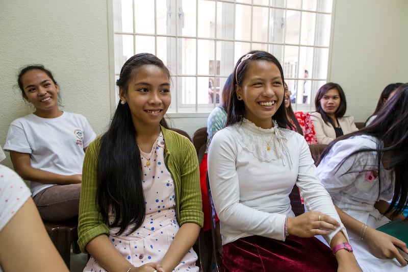Young women in the Philippines sit in class together and smile.