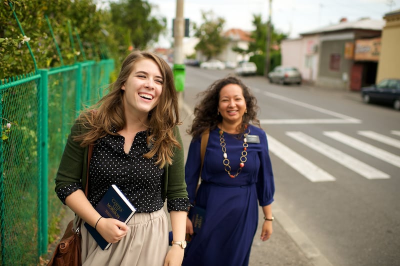 Two sister missionaries in Romania laugh while walking down a street together.