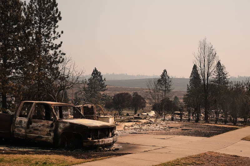 A burned truck sits in a driveway near several destroyed homes in a residential neighborhood Tuesday, Aug. 4, 2026, after a wildfire hit the northern part of Spokane, Washington.