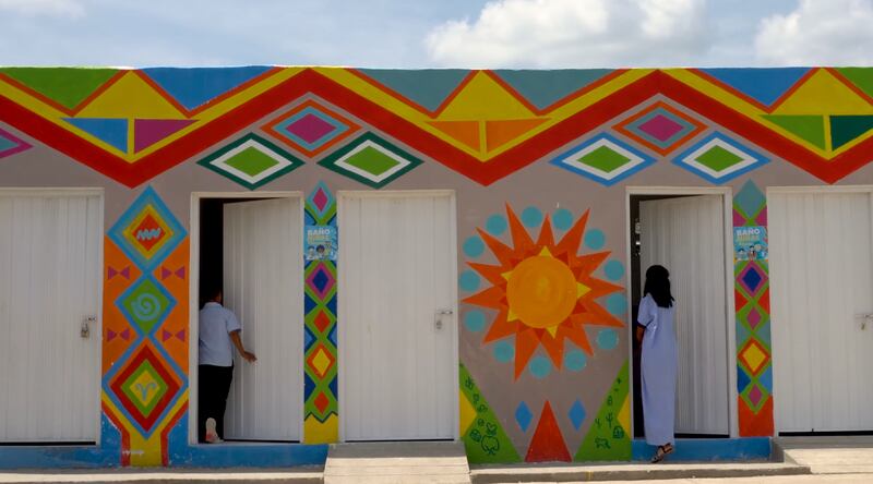 Two Wayúu community youth enter a new building with toilets, faucets, and sinks after they were painted in the Kanaas style in Guajira, Colombia, in February 2024.