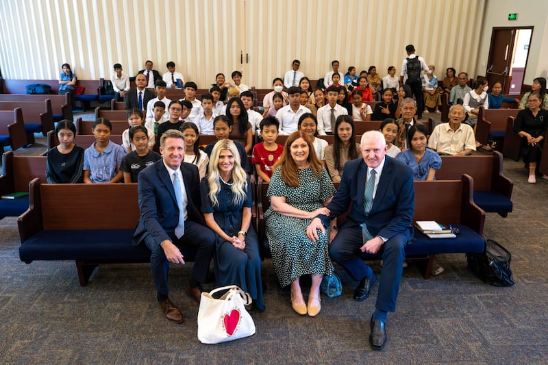 Young Men General President Timothy L. Farnes, left, his wife, Sister Linsey Farnes, Sister Terri Johnson and her husband, Elder Kelly R. Johnson, a General Authority Seventy and president of the Asia Area, take a photo with youth in Cambodia after a devotional in May 2026.