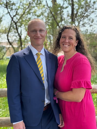 Glenn and Erica Nielson stand outside together in front of trees and a fence.