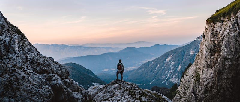 A hiker pauses while hiking Mangart Peak in Slovenia at sunrise.
