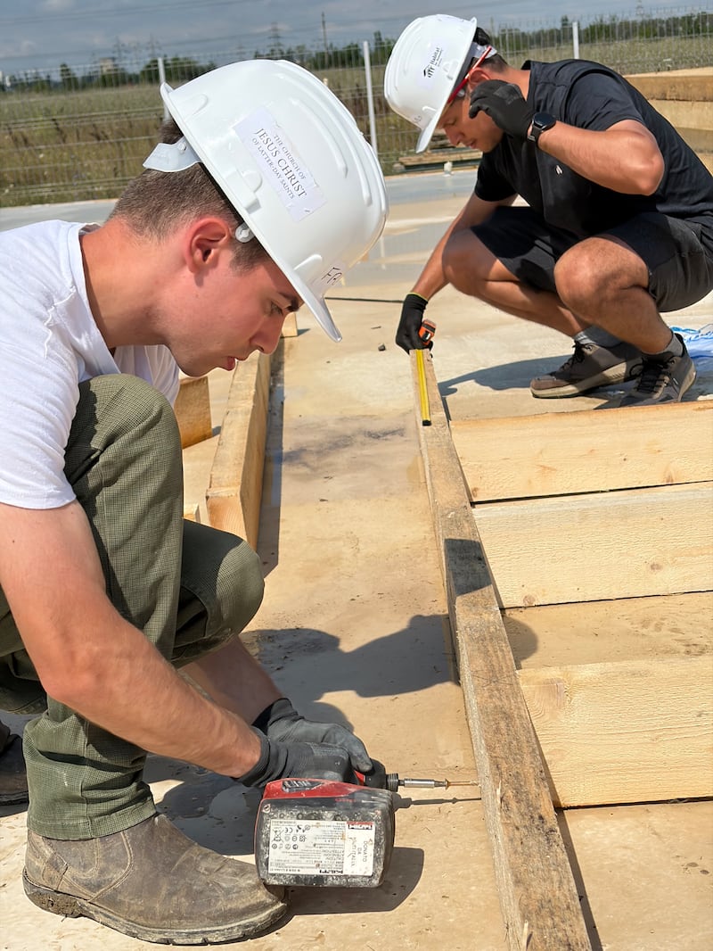 Young adults measure and assemble wooden wall frames for homes under construction for a Habitat for Humanity Romania service project in Berceni, Romania, in August 2026.