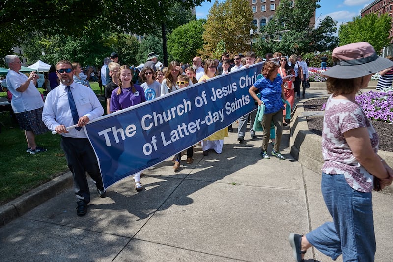 Dozens of members of The Church of Jesus Christ of Latter-day Saints hold a sign saying the Church’s name at the 11th Annual Indy Festival of Faiths in Indianapolis, Indiana.