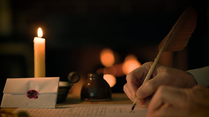 A man writes a letter using a quill pen, with a fire in the background.