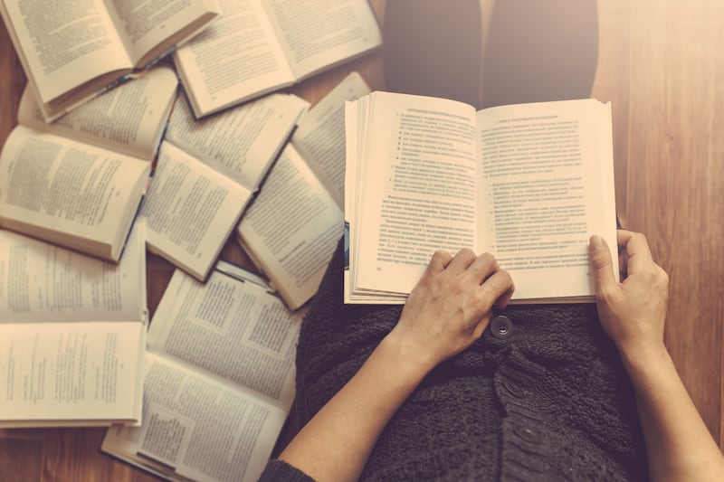 Woman reads a book with several books on the floor around her.