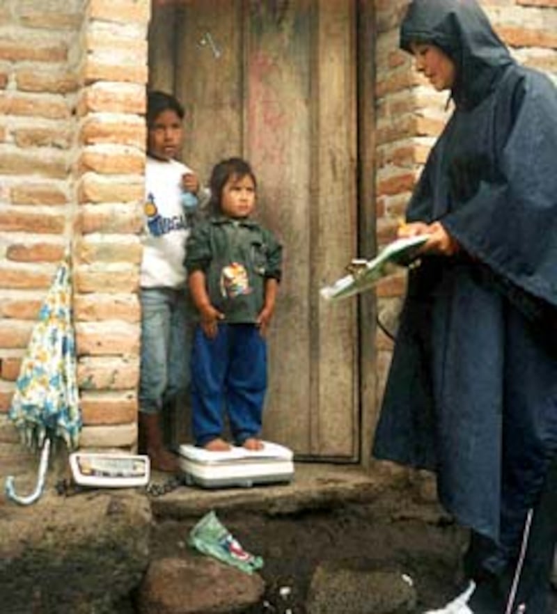 An international student weighs children in Ecuador to assess needs as part of university thesis.