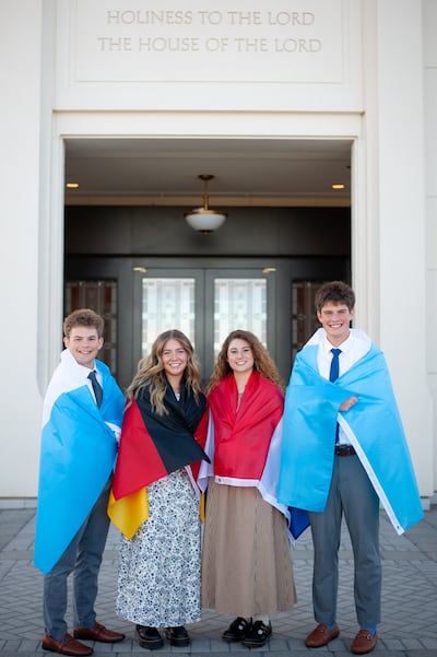 Isaac, Elle, Isabel and Eli Reid pose for a picture with flags representing where they will serve missions draped around their shoulders.