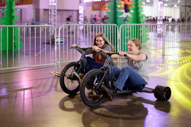 Two women participate in a Tricycle race at the Salt Palace Convention Center during the 2026 Utah Area YSA Conference in Salt Lake City on Friday, Aug. 14, 2026.