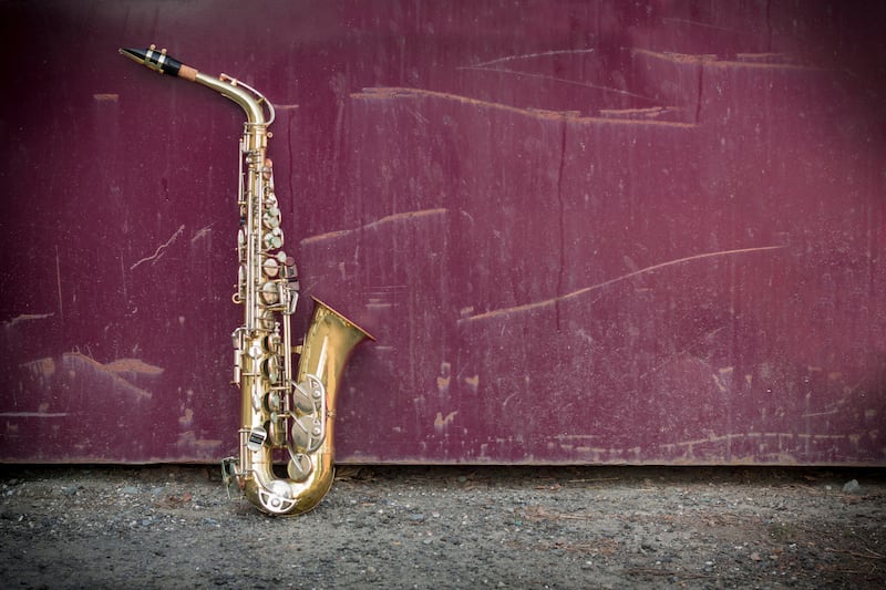 Alto saxophone sits on the ground, propped up against a red wall.