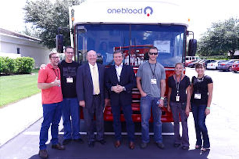 Rick Walsh and Elder Rulon Munns welcome young single adults to "The Big Red Bus" to donate blood.