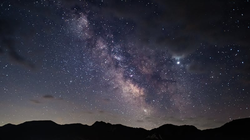 The Milky Way is seen over mountain peaks.