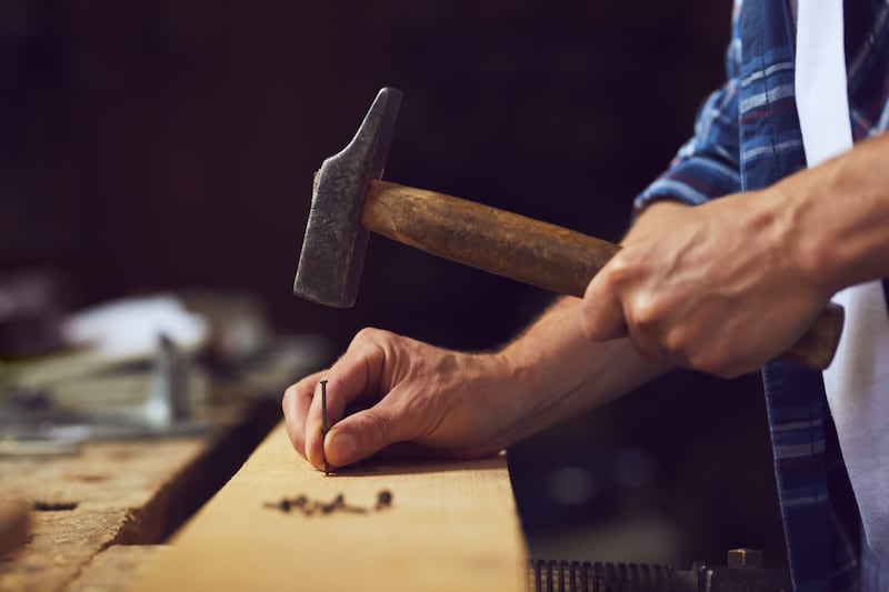 A carpenter hammers a nail into wooden plank in a shop.