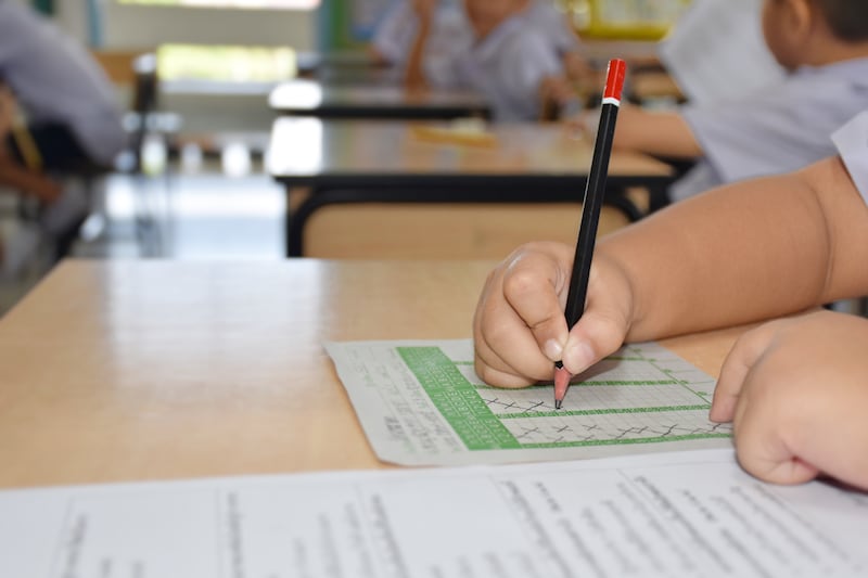 An elementary school-age student writes with a pencil on test while at school.
