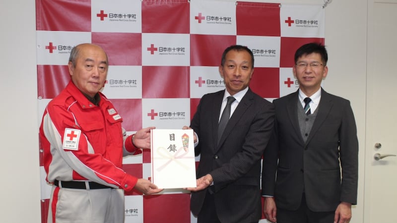 Two Church leaders wearing a suit and tie hand a certificate to an official from the Japanese Red Cross Society.