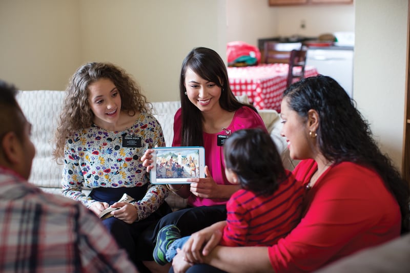 Two sister missionaries teach a family in their home.