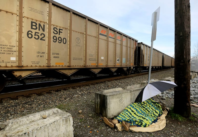 A homeless person sleeps as a freight train passes in Puyallup, Wash., on Saturday, Jan. 25, 2020.