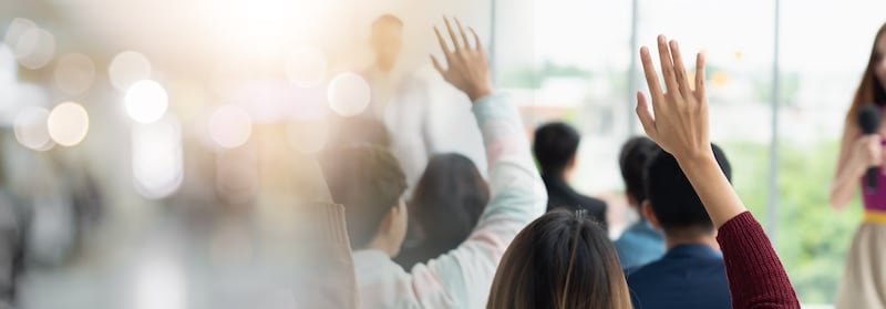 People raise their hands during a large group meeting.