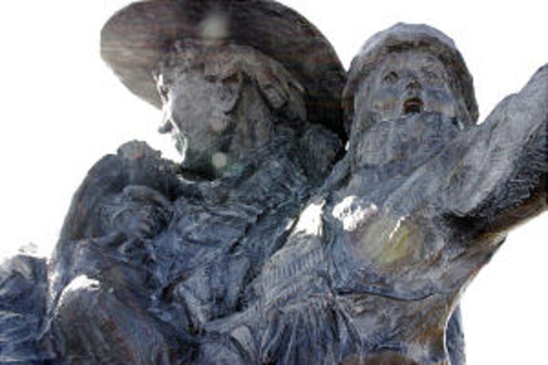 Detail of statue depicting man carrying a child with an infant tucked under his coat.