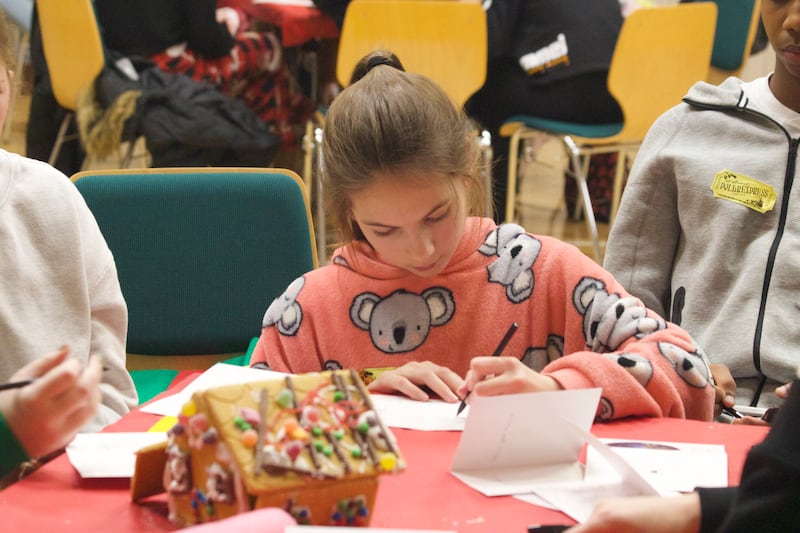 Youth in the Northampton England Stake write cards at a table to send to others as part of a service activity in December 2024.