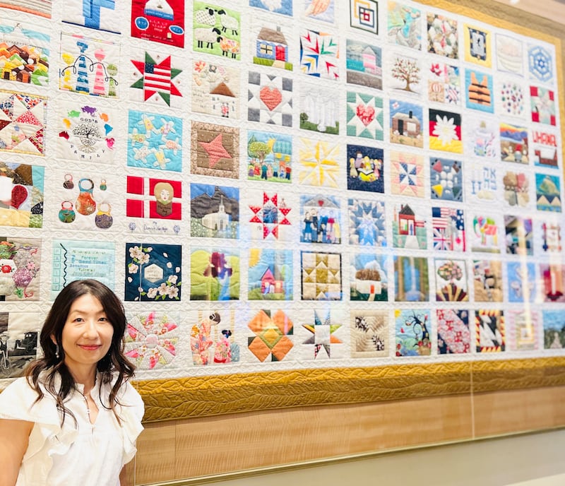 Sachiko Aldous stands by "The Family Quilt" display at the Temple Square Visitors' Center in Salt Lake City, July 2026.