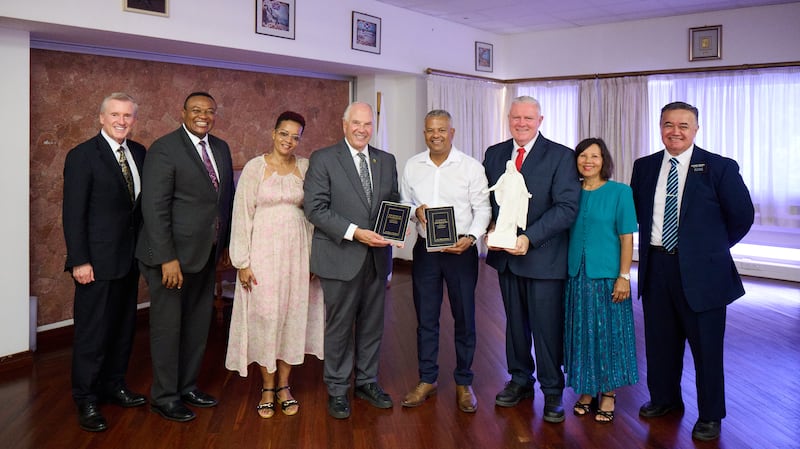 Elder Ronald A. Rasband stands with Sebastien Pillay, the vice president of Seychelles, as they hold two copies of the Book of Mormon, in Victoria, Seychelles, Oct. 29, 2025. Also pictured are Elder Kevin R. Duncan, Elder Thierry K. Mutombo, Deborah Maimee, Elder Evan Healy and Sister Marie Healy, and Kenya Nairobi East Mission President David T. Onekawa.