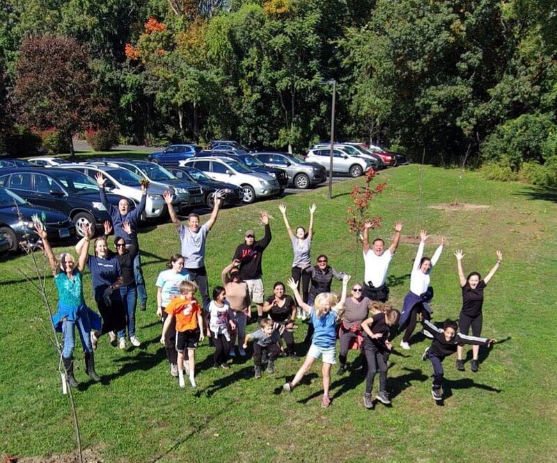 About two dozen members of the Fairfield Connecticut Stake jump on a grassy field for a drone shot of their tree-planting efforts.