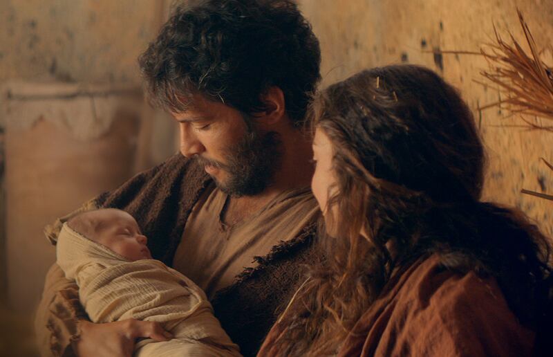 Joseph sits next to Mary while he holds baby Jesus after His birth.