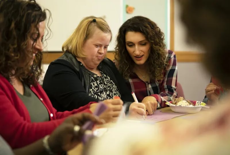 Two women — one of whom has Down syndrome — write in a card.