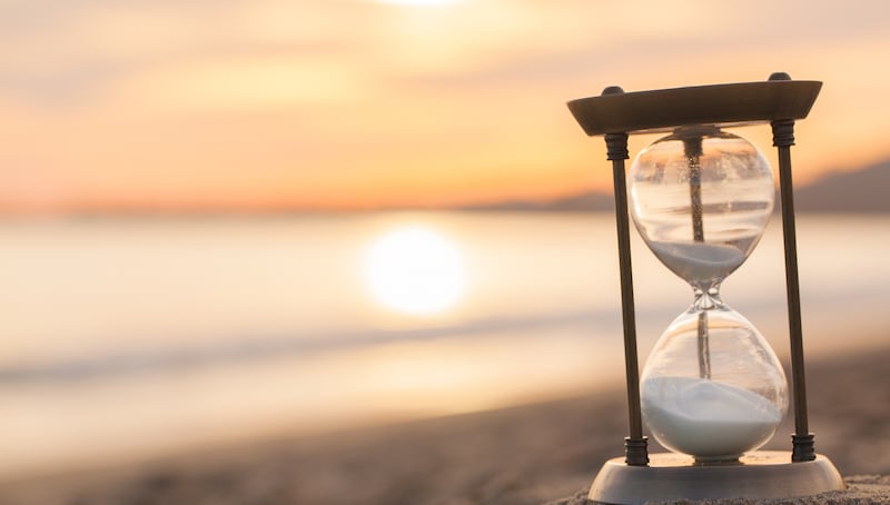 An hourglass is on the beach as the sun rises.