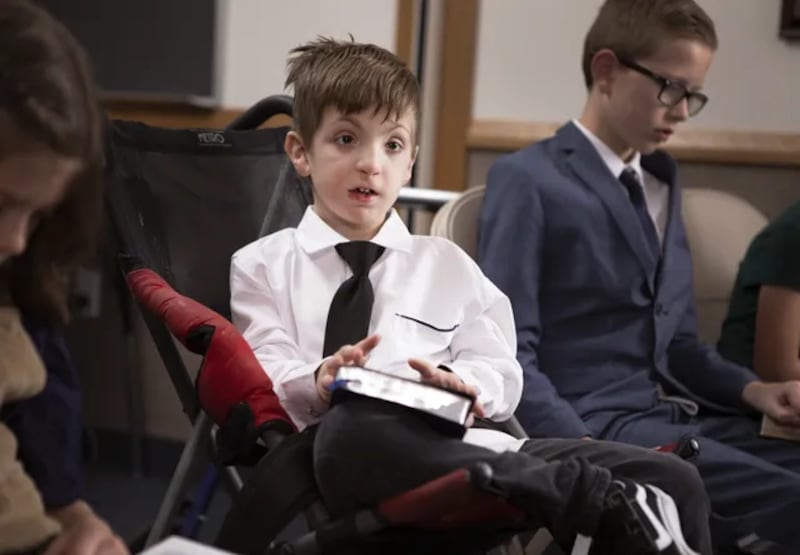 A boy in a wheelchair holds scriptures during a Primary class.