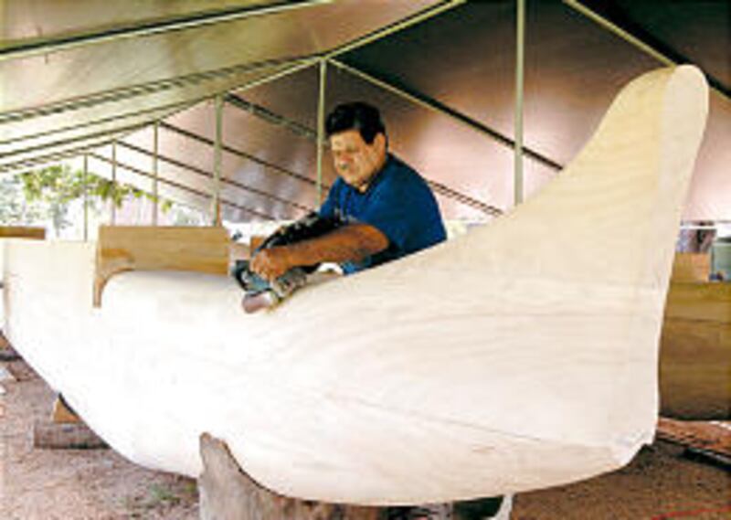 Brother Pulotu checks sanded surface of new canoe.
