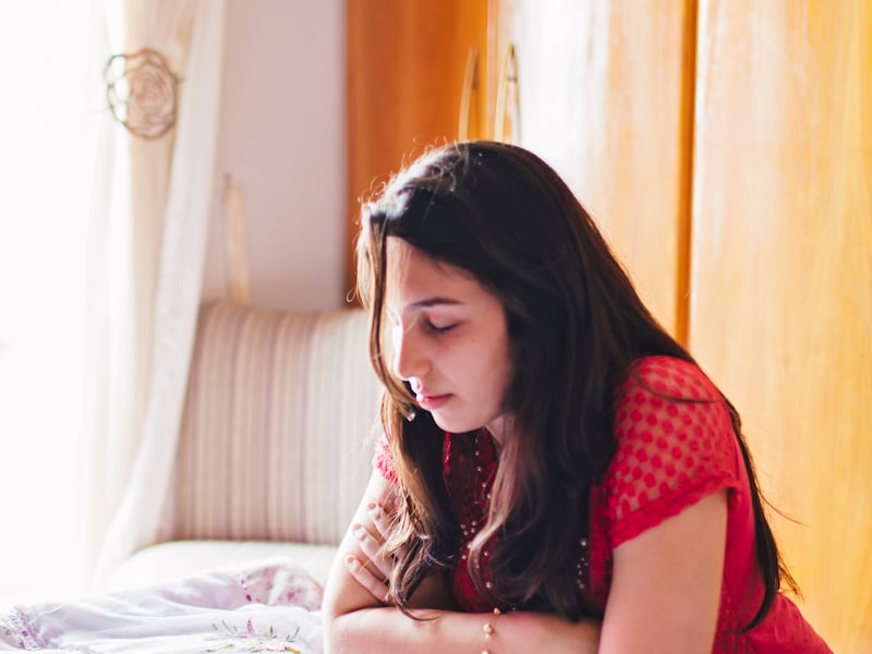 A young woman prays at her bedside.