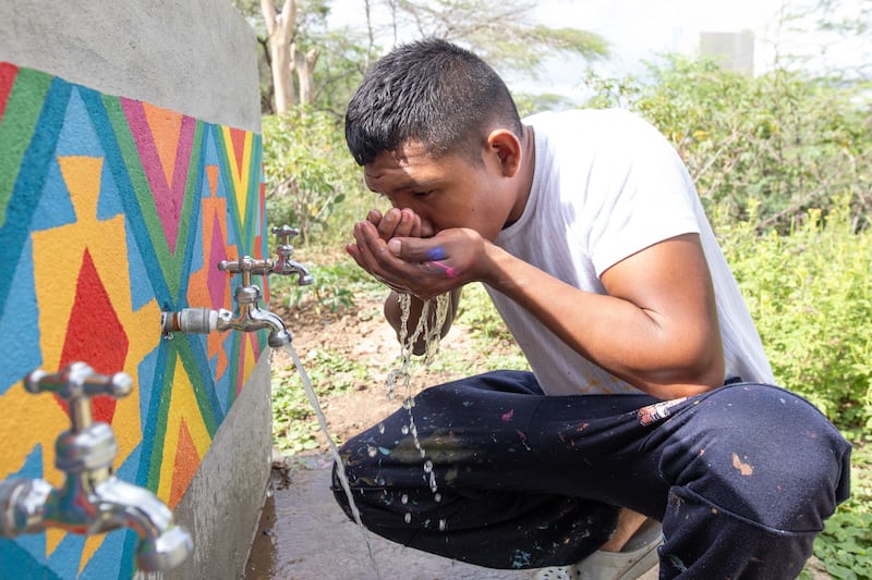 Keiber Epinayu, a young artist and Wayúu community leader, drinks water from a new faucet after painting the infrastructure in La Guajira, Colombia, in February 2024.