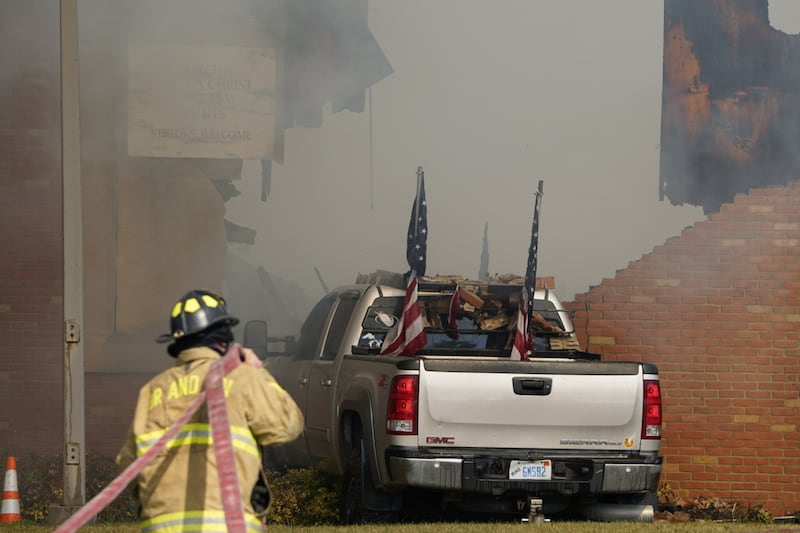 A vehicle that was rammed into the Grand Blanc Ward building is surrounded by smoke as a firefighter works on the scene in Grand Blanc, Michigan, Sunday, Sept. 28, 2025.