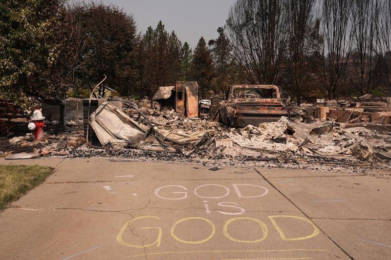A "God is good" sign is written in chalk next to a fire hydrant and a burned house after a wildfire hit the northwest part of Spokane, Washington, Tuesday, Aug. 4, 2026.
