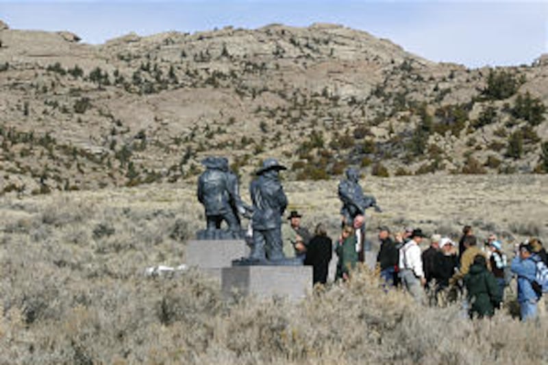 Visitors gather around statues honoring pioneer rescuers with Martin's Cove in the background.