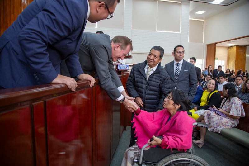 Elder Gary E. Stevenson of the Quorum of the Twelve Apostles reaches down to shake the hand of a sister in a wheelchair and greet other attendees.